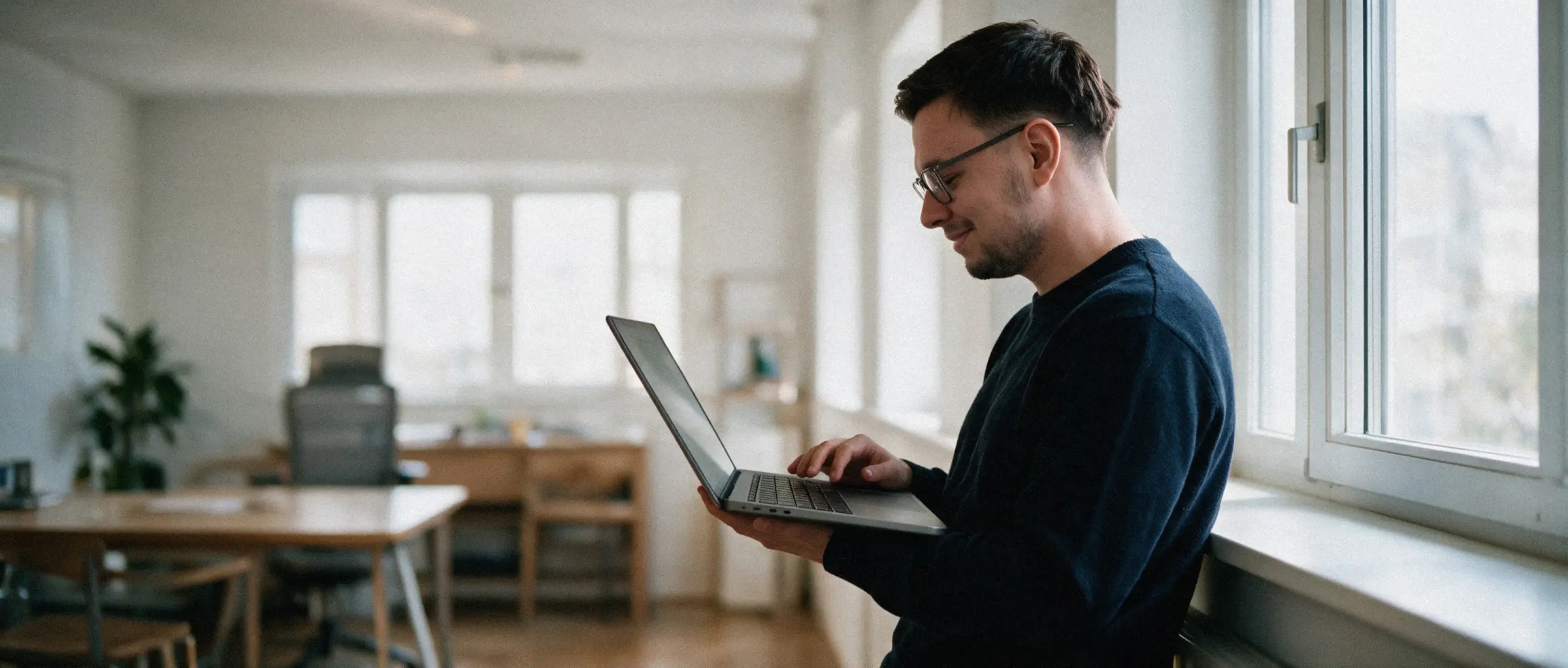 Alex Dreger lehnt mit dem Laptop am Bürofenster