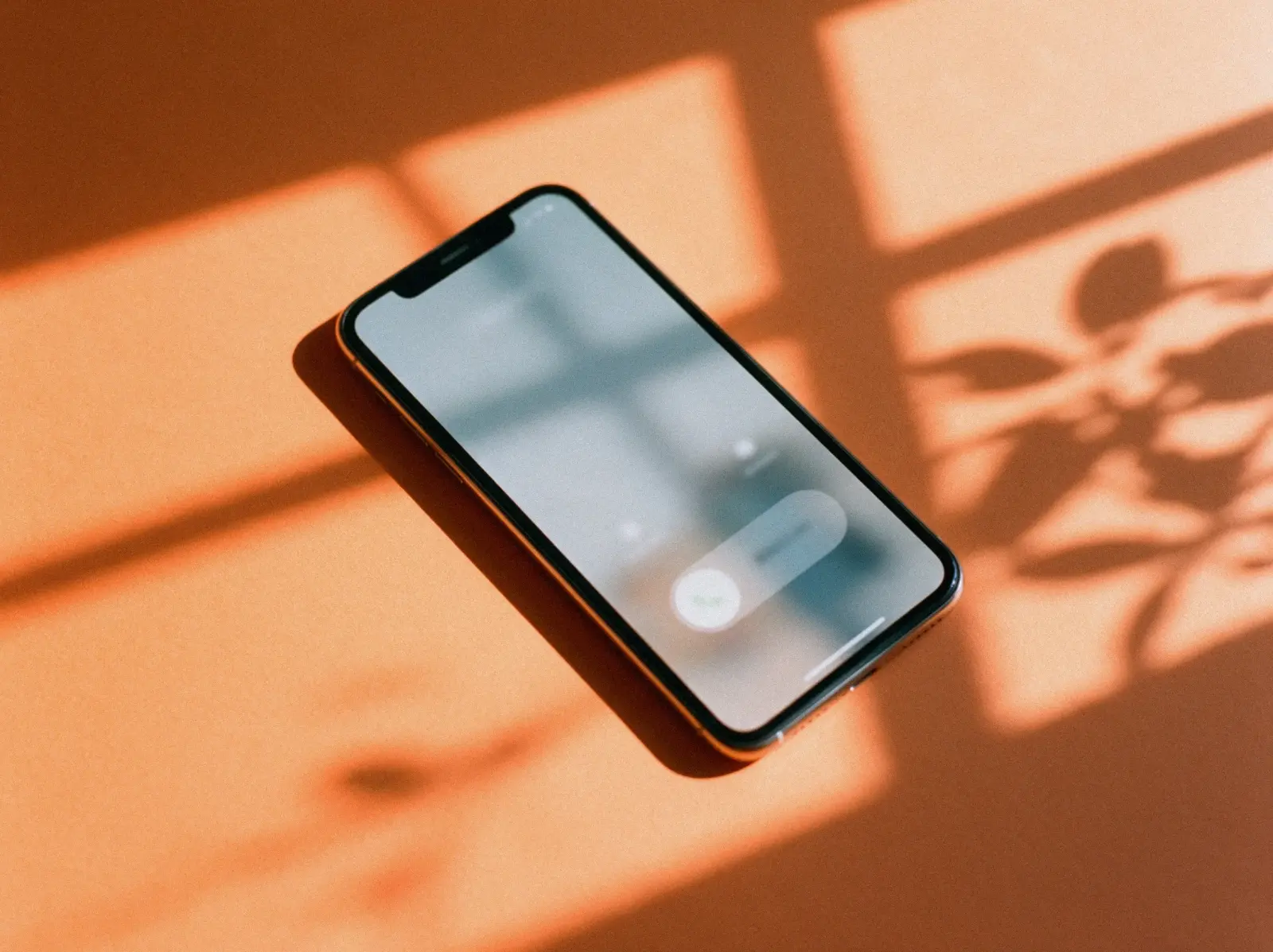Smartphone mit eingehendem Anruf auf apricotfarbenem Papier, darüber der Schatten eines Fensters und von Blättern