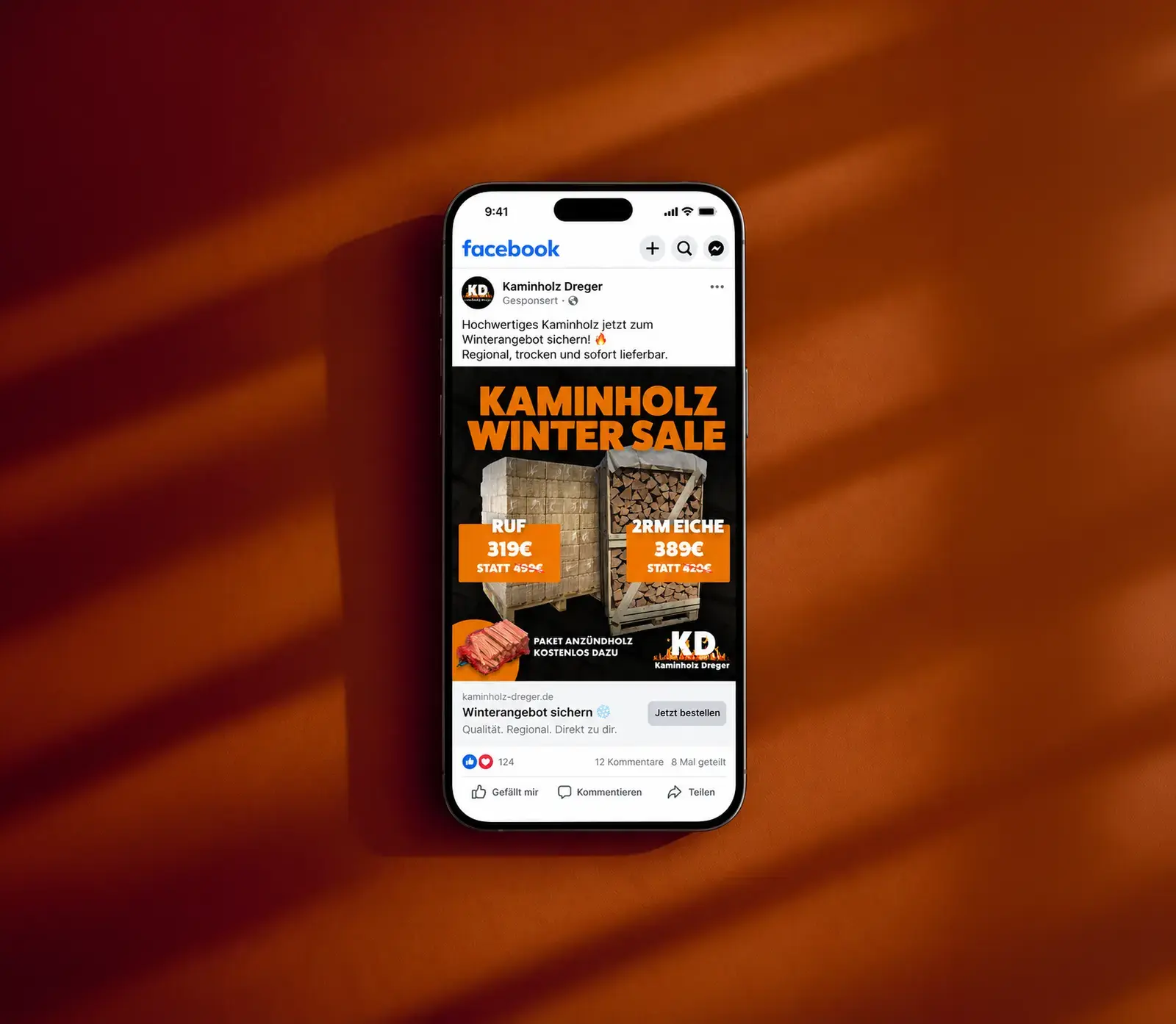 Smartphone mit einer Facebook-Anzeige von Kaminholz Dreger: Winter Sale für Kaminholz, davor ein orangefarbener Hintergrund